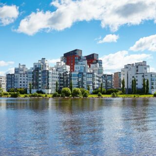 Vybild över Lillåudden och dess fastigheter. Moderna hyreshus i olika storlekar och färger på fasaderna. Grönområden och Mälaren omger.