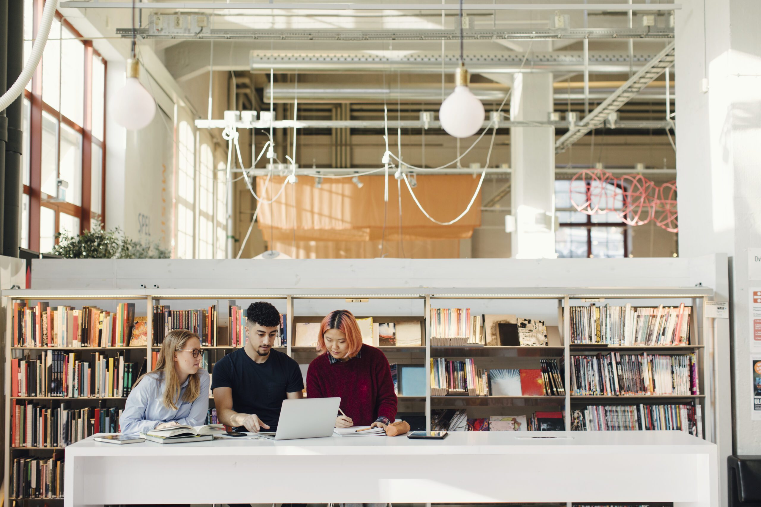 Tre studenter i ett bibliotek tittar på en dator